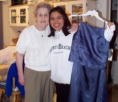 Picture of Scott's dainty white haired grandma and Elysia with arms around each other, heads touching,  big smiles and Elysia holding up a two piece shimmering dark blue bride's dress on a hanger. (160917 bytes)