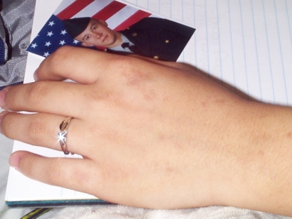 Close-up shot of Elysia's hand with engagement ring on a ruled writing notebook with Scott's Army picture on the pad, ready to write a letter to Scott.